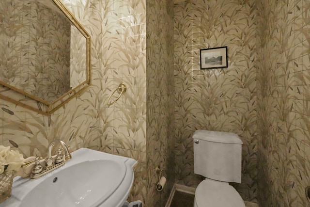 bathroom featuring a sink, toilet, and wallpapered walls