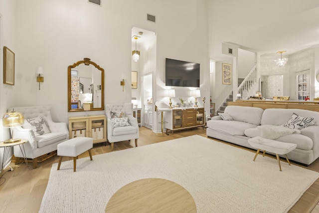 living room featuring visible vents, a chandelier, stairs, a towering ceiling, and wood finished floors