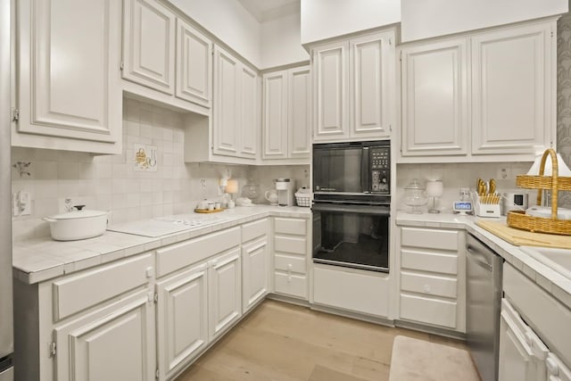 kitchen featuring light wood-type flooring, tile counters, black microwave, dishwasher, and tasteful backsplash