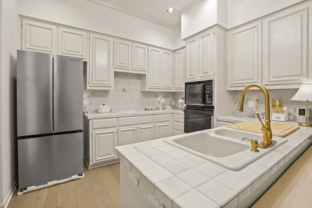 kitchen with tile counters, light wood-type flooring, a peninsula, white cabinets, and black appliances