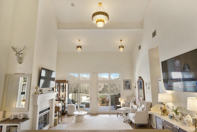 living area with a notable chandelier, a fireplace with flush hearth, visible vents, and a towering ceiling