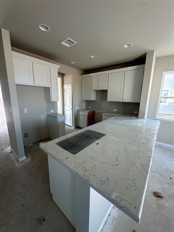 kitchen with backsplash, kitchen peninsula, light stone countertops, and white cabinets