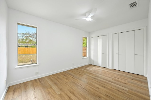 unfurnished bedroom with light hardwood / wood-style flooring, multiple windows, multiple closets, and ceiling fan