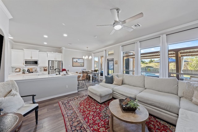 living room with ceiling fan with notable chandelier, dark hardwood / wood-style flooring, and ornamental molding