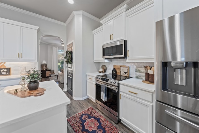 kitchen with dark wood-type flooring, stainless steel appliances, tasteful backsplash, crown molding, and white cabinets