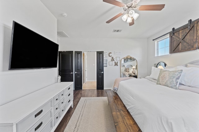 bedroom featuring a barn door, ceiling fan, and dark hardwood / wood-style floors