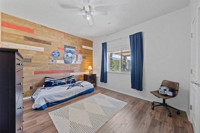 bedroom featuring hardwood / wood-style floors, ceiling fan, and wood walls