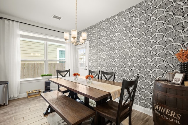 dining space featuring wallpapered walls, baseboards, visible vents, an inviting chandelier, and light wood-style floors