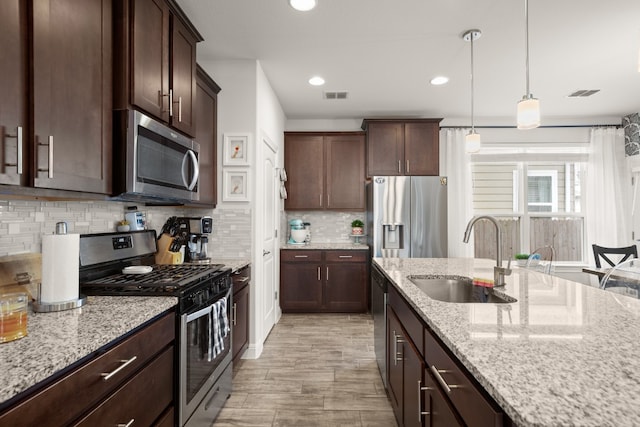 kitchen featuring visible vents, appliances with stainless steel finishes, light stone counters, decorative light fixtures, and a sink