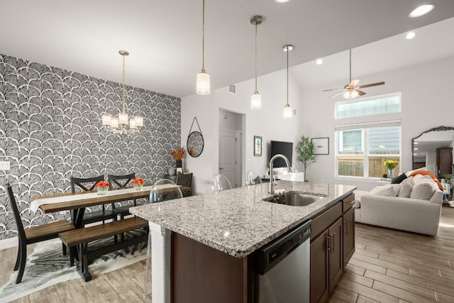 kitchen with light wood-type flooring, stainless steel dishwasher, ceiling fan with notable chandelier, dark brown cabinetry, and sink