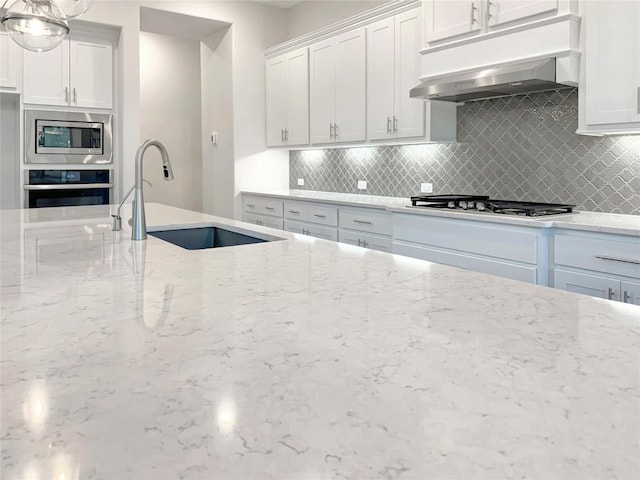 kitchen featuring a sink, range hood, appliances with stainless steel finishes, light stone countertops, and tasteful backsplash