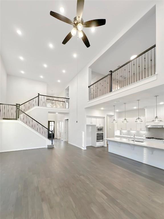 unfurnished living room with a high ceiling, dark hardwood / wood-style floors, ceiling fan, and sink