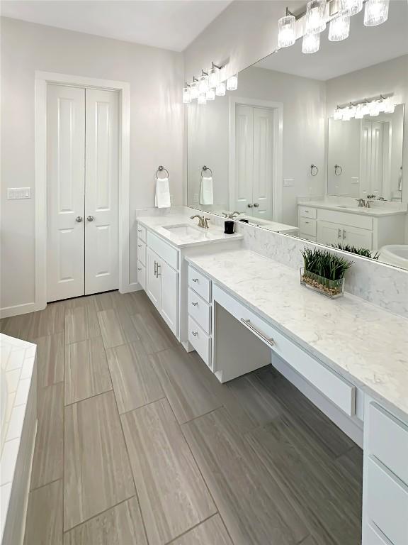 full bath with wood finish floors, two vanities, a sink, and baseboards