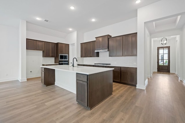 347 Five Mile Creek Way, Kyle, TX 78640 - kitchen featuring appliances with stainless steel finishes, a sink, a center island with sink, decorative backsplash, and dark brown cabinets