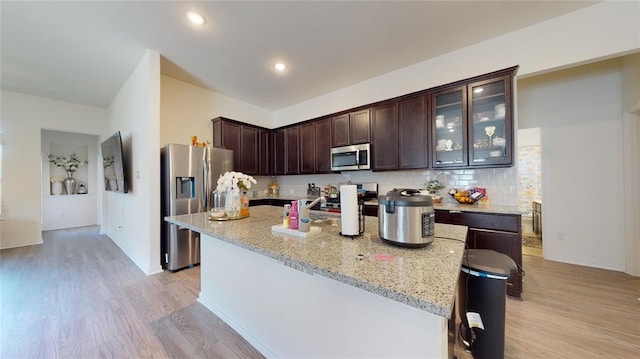 kitchen featuring stainless steel appliances, light stone counters, light wood-type flooring, dark brown cabinetry, and a kitchen island with sink