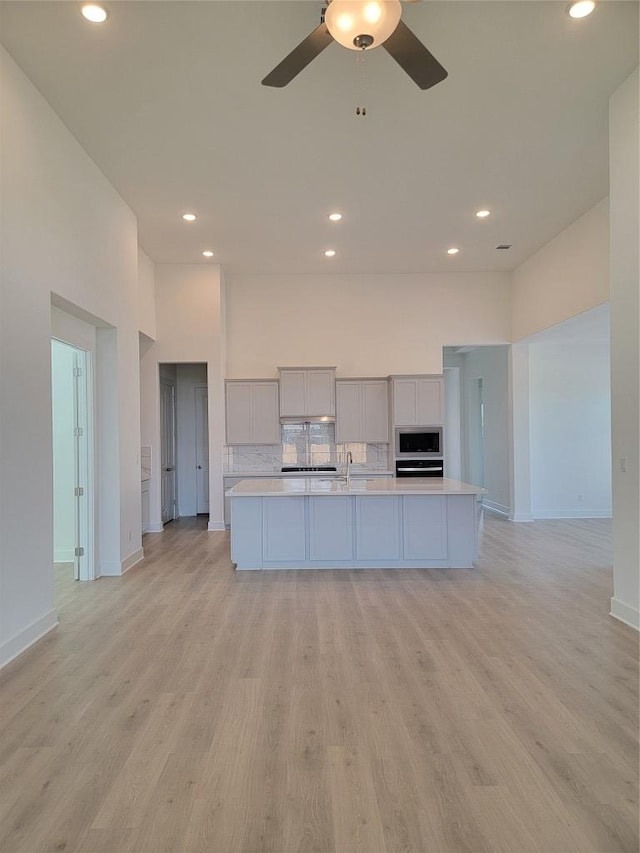 kitchen with stainless steel microwave, light countertops, backsplash, a ceiling fan, and baseboards