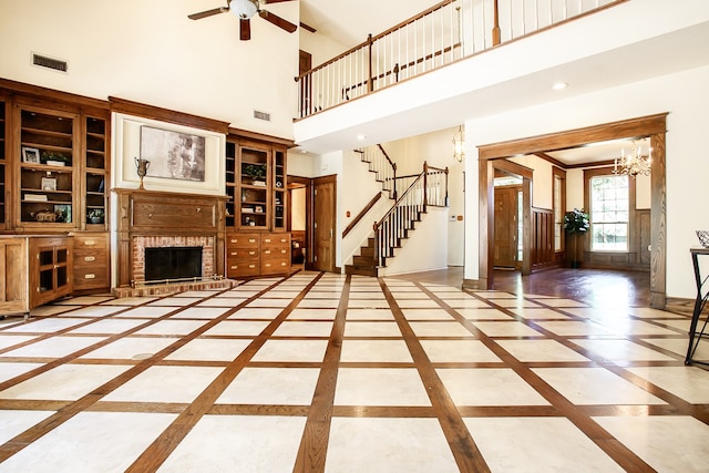 unfurnished living room with a fireplace, a towering ceiling, and ceiling fan with notable chandelier