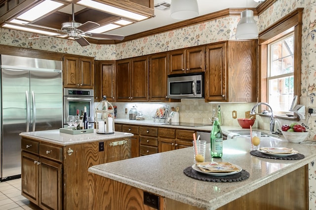 kitchen with light stone countertops, a center island, ceiling fan, stainless steel appliances, and sink