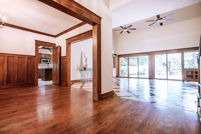 unfurnished living room with a towering ceiling, dark hardwood / wood-style floors, ceiling fan, and ornamental molding