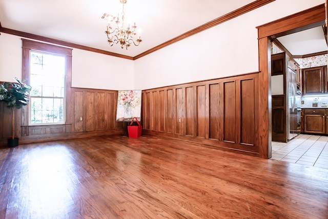 empty room with ornamental molding, light hardwood / wood-style floors, and a notable chandelier