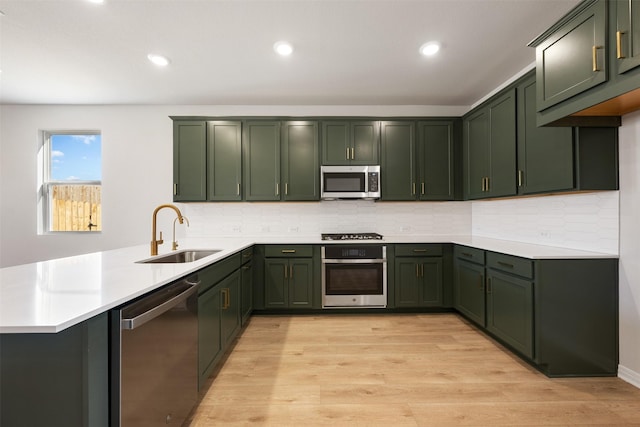 kitchen with green cabinetry, sink, kitchen peninsula, stainless steel appliances, and light wood-type flooring