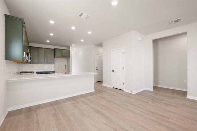 kitchen featuring sink, light hardwood / wood-style flooring, backsplash, green cabinetry, and kitchen peninsula