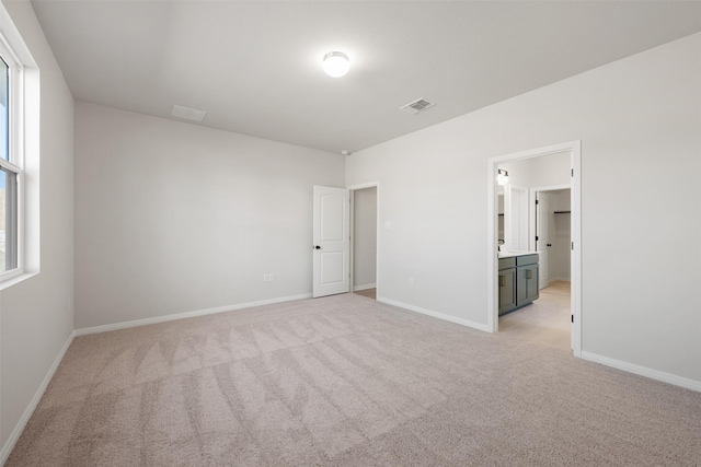 unfurnished bedroom featuring ensuite bathroom and light carpet