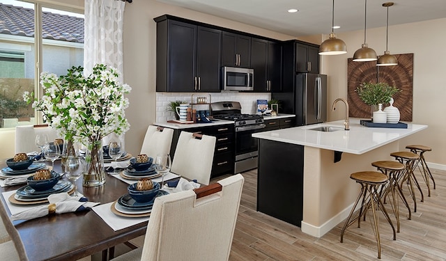 kitchen with sink, hanging light fixtures, stainless steel appliances, light hardwood / wood-style floors, and a kitchen island with sink