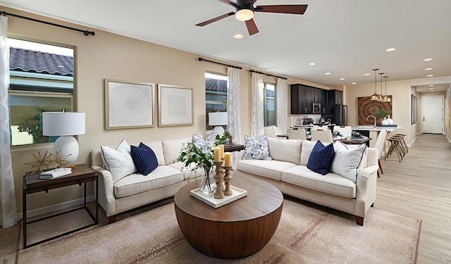 living room featuring ceiling fan, sink, and light wood-type flooring