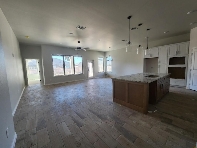 kitchen featuring white cabinetry, ceiling fan, gas stovetop, light stone counters, and a kitchen island