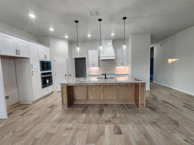 kitchen with custom exhaust hood, white cabinetry, light stone counters, and hanging light fixtures