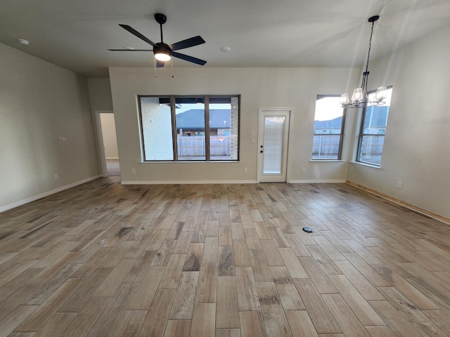 spare room featuring ceiling fan with notable chandelier, a healthy amount of sunlight, and light hardwood / wood-style flooring