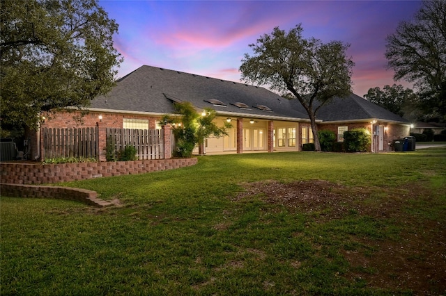 back house at dusk featuring a lawn