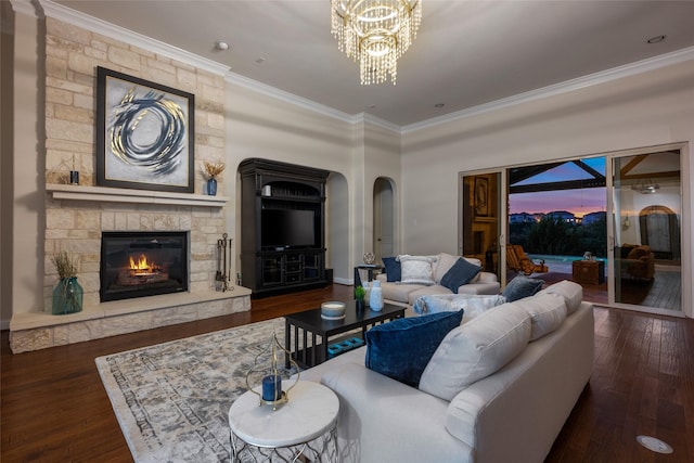 living room with dark wood-type flooring, crown molding, a stone fireplace, and an inviting chandelier