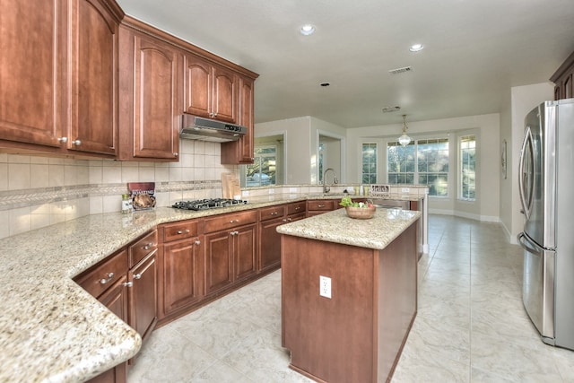 kitchen with a center island, hanging light fixtures, stainless steel appliances, light stone counters, and decorative backsplash