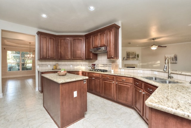 kitchen featuring ceiling fan with notable chandelier, a kitchen island, light stone countertops, and sink