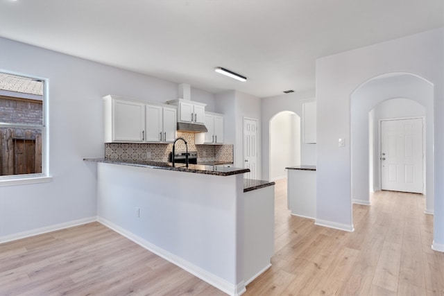 kitchen with kitchen peninsula, light wood-type flooring, tasteful backsplash, dark stone countertops, and white cabinets