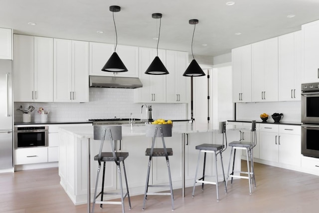 kitchen featuring hardwood / wood-style floors, pendant lighting, appliances with stainless steel finishes, and an island with sink