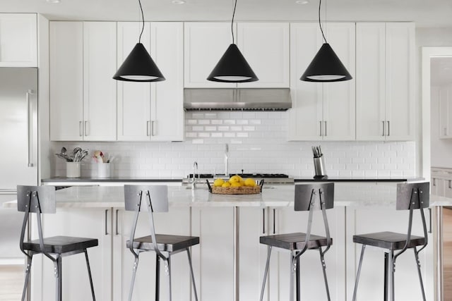 kitchen featuring a kitchen breakfast bar, decorative backsplash, white cabinets, and hardwood / wood-style flooring