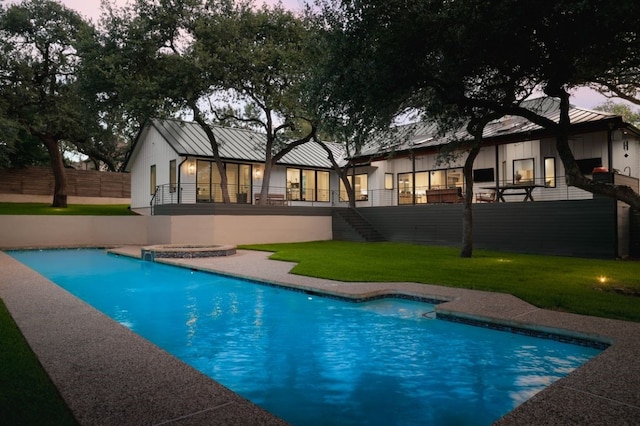 4101 Mcbrine Pl, Austin, TX 78746 - back of property at dusk featuring a jacuzzi, stairs, a standing seam roof, and an outdoor pool