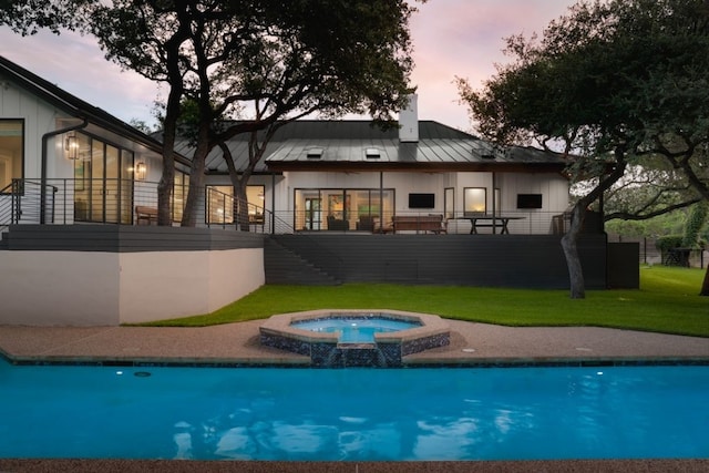 back house at dusk with a yard and a pool with hot tub