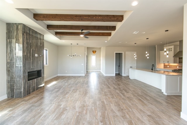 unfurnished living room featuring beam ceiling, ceiling fan with notable chandelier, light hardwood / wood-style floors, and sink