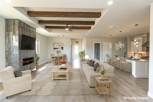 living room featuring sink, ceiling fan, light hardwood / wood-style floors, beam ceiling, and a large fireplace