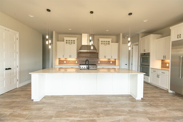 kitchen featuring a large island with sink, white cabinets, wall chimney exhaust hood, and pendant lighting