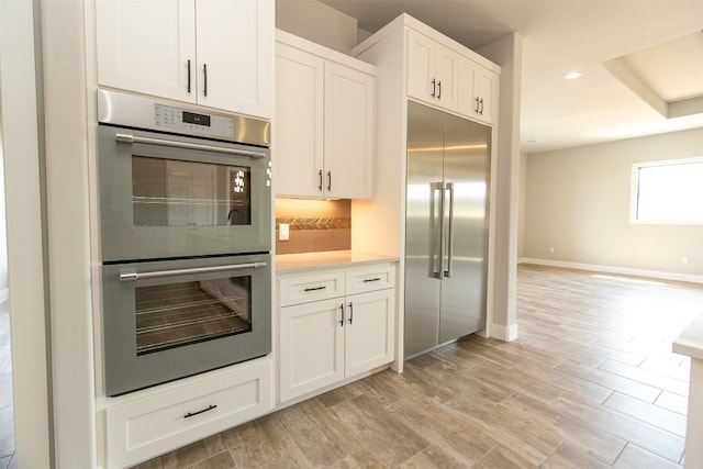 kitchen featuring white cabinets, decorative backsplash, light wood-type flooring, and appliances with stainless steel finishes