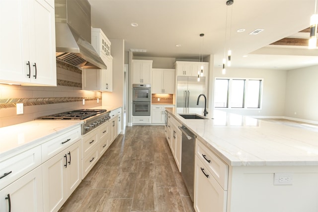 kitchen featuring sink, wall chimney exhaust hood, stainless steel appliances, pendant lighting, and a spacious island