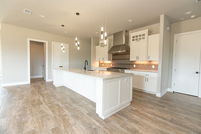 kitchen with pendant lighting, wall chimney exhaust hood, a spacious island, and white cabinetry