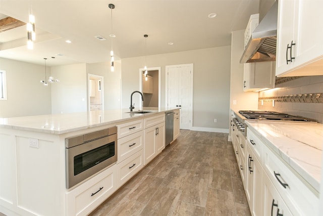 kitchen with decorative light fixtures, white cabinetry, stainless steel appliances, and wall chimney range hood