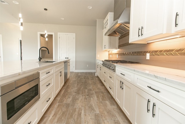 kitchen with sink, wall chimney exhaust hood, decorative light fixtures, white cabinets, and appliances with stainless steel finishes