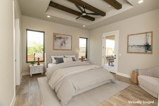 bedroom with beamed ceiling, light hardwood / wood-style floors, ceiling fan, and a tray ceiling